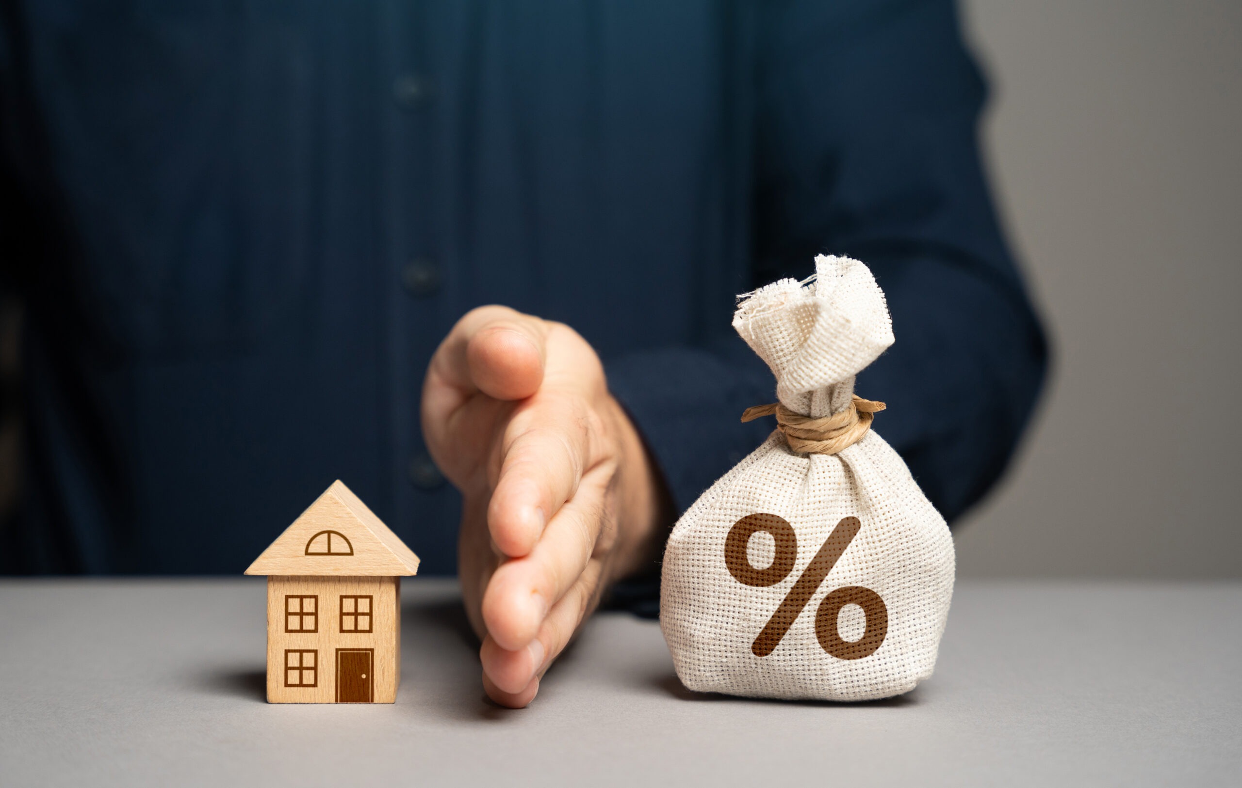 Wooden house model next to a money bag symbolizing mortgage interest
